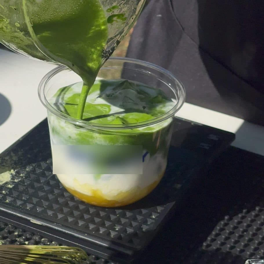 Bright matcha poured from a jug straight into a clear cup, over milk and ice.